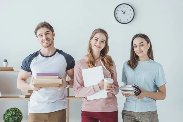 Smiling students holding books, laptop, coffee and copybooks — Stock Photo