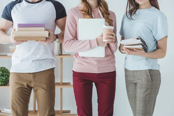Cropped view of students holding books, laptop, coffee and copybooks — Stock Photo