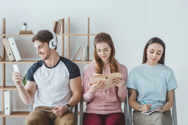 Jeunes étudiants écoutant de la musique, lisant des livres et écrivant dans des copybooks — Photo de stock