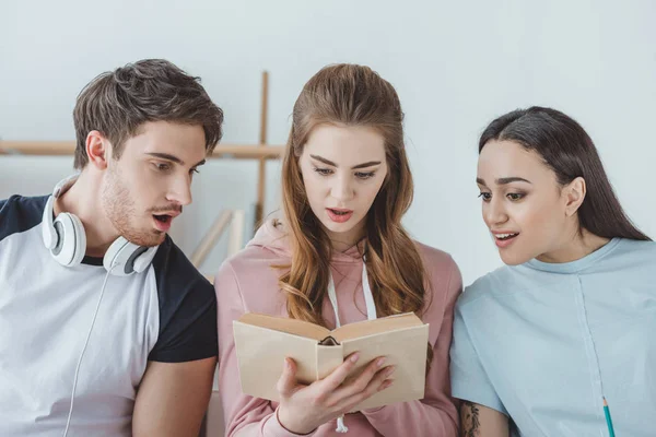 Shocked young students reading one book — Stock Photo