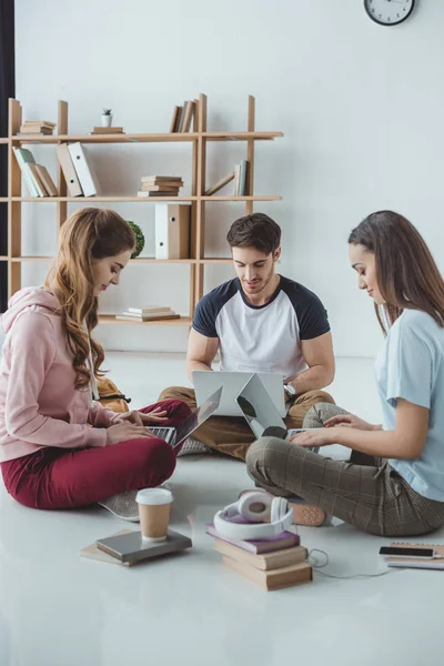 Jóvenes estudiantes que estudian con ordenadores portátiles, libros y café en el suelo - foto de stock