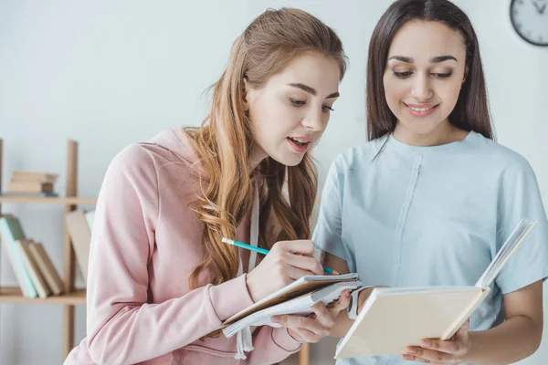 Meninas multiculturais escrevendo algo enquanto estudam com livro — Fotografia de Stock