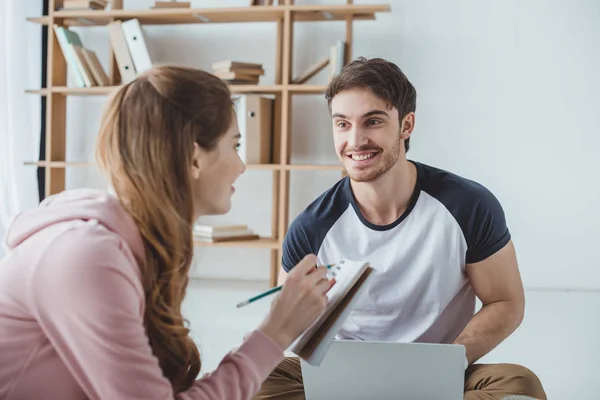 Пара молодих студентів, які використовують ноутбук і пишуть у книзі — Stock Photo