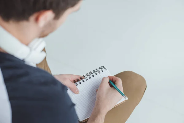 Visão recortada de estudante do sexo masculino com fones de ouvido escrevendo em notebook — Fotografia de Stock