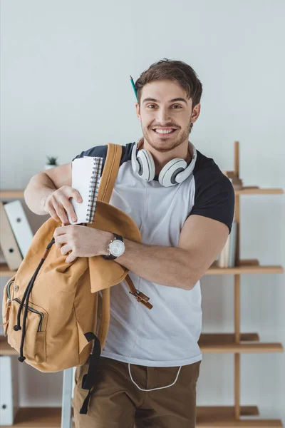 Улыбающийся студент с наушниками, рюкзаком и ноутбуком — стоковое фото