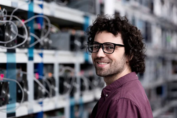 Feliz joven ingeniero informático en la granja minera criptomoneda mirando a la cámara - foto de stock