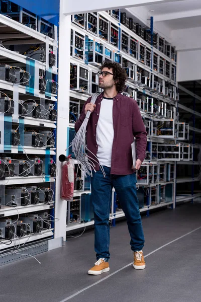 Jeune ingénieur informatique avec fils Ethernet sur l'épaule à la ferme minière crypto-monnaie — Photo de stock