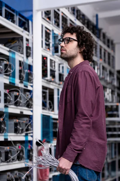 Jeune ingénieur informatique avec fils Ethernet à la ferme minière crypto-monnaie — Photo de stock