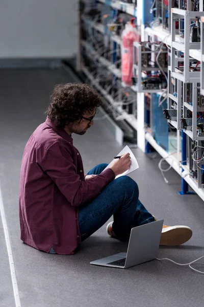 Engenheiro de computação trabalhando enquanto sentado no chão na fazenda de mineração criptomoeda — Fotografia de Stock