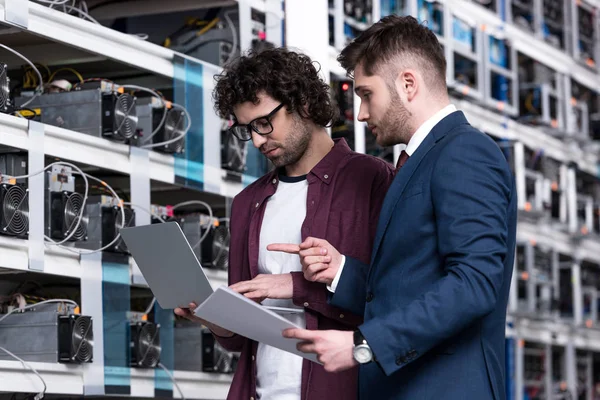 Homme d'affaires et ingénieur informatique travaillant avec ordinateur portable ensemble à la ferme minière Bitcoin — Photo de stock