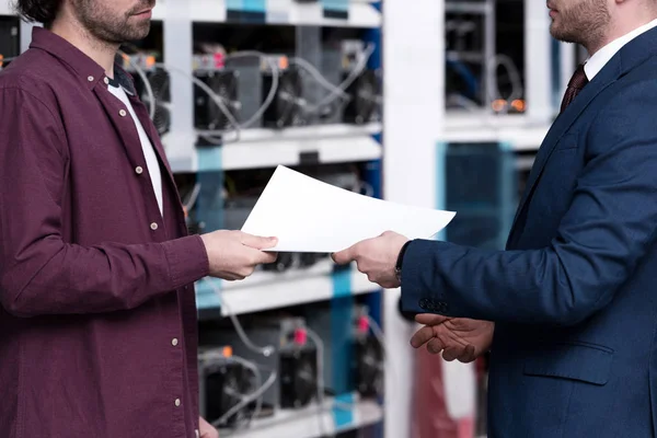 Cropped shot of businessman and computer engineer passing documents at cryptocurrency mining farm — Stock Photo