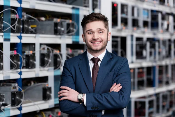 Jeune homme d'affaires souriant avec les bras croisés à la ferme minière crypto-monnaie — Photo de stock