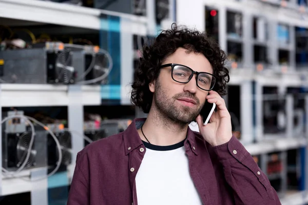Handsome computer engineer talking by phone at ethereum mining farm — Stock Photo