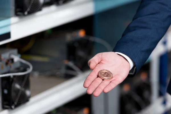 Recortado tiro de hombre de negocios en traje celebración de bitcoin en la granja minera criptomoneda - foto de stock