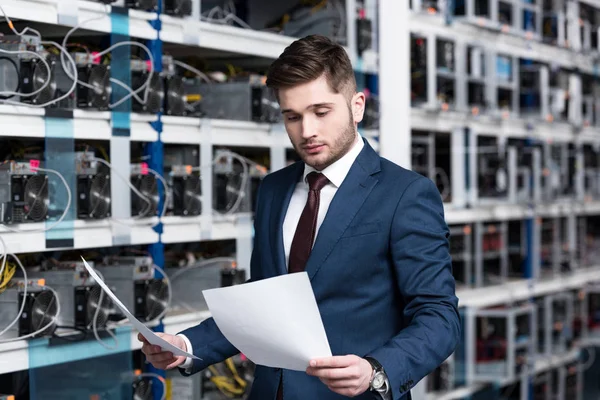 Bonito jovem empresário lendo documentos de negócios na fazenda de mineração criptomoeda — Fotografia de Stock