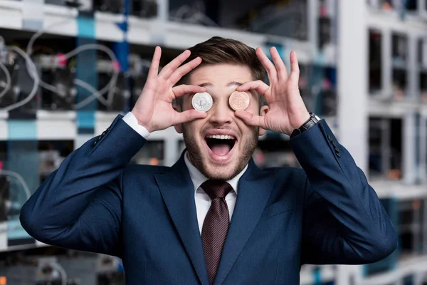 Feliz joven empresario cubriendo los ojos con bitcoins en la granja minera criptomoneda - foto de stock