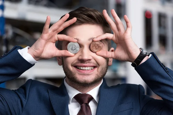 Souriant jeune homme d'affaires couvrant les yeux avec Bitcoins à la ferme minière crypto-monnaie — Photo de stock