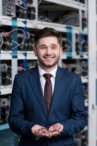 Feliz joven empresario con un montón de bitcoins en las manos en la granja minera criptomoneda - foto de stock