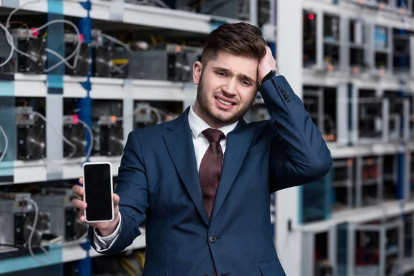 Failed young businessman showing smartphone at cryptocurrency mining farm — Stock Photo