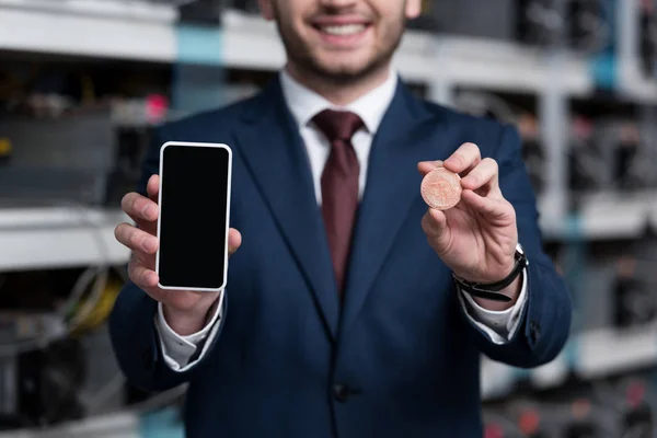 Cropped shot of businessman showing smartphone and bitcoin at cryptocurrency mining farm — Stock Photo