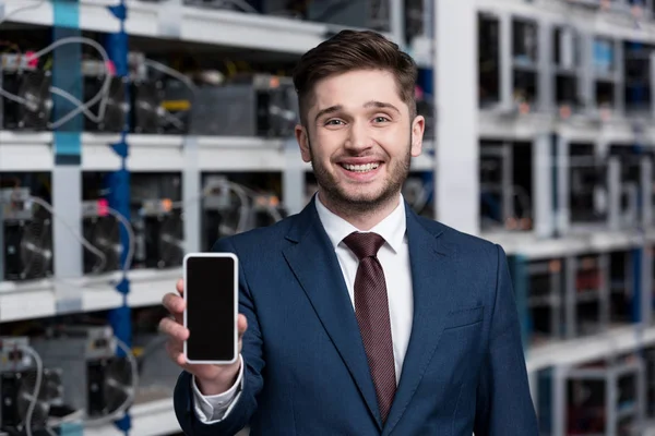 Happy young businessman showing smartphone at cryptocurrency mining farm — Stock Photo