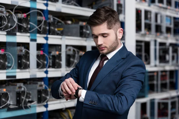 Handsome young businessman looking at wristwatch at ethereum mining farm — Stock Photo