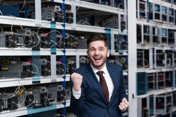 Happy young businessman celebrating victory and raising fist at cryptocurrency mining farm — Stock Photo