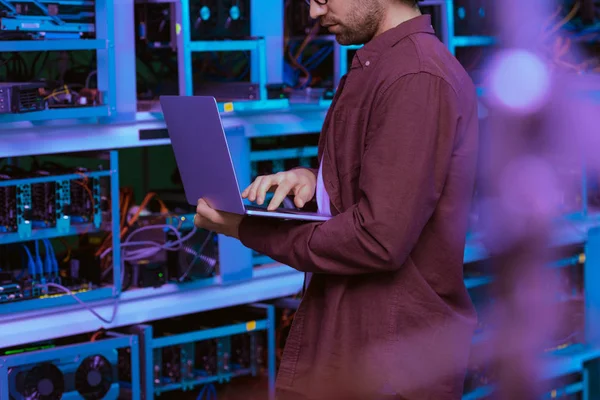 Cropped shot of young computer engineer working with laptop at ethereum mining farm — Stock Photo