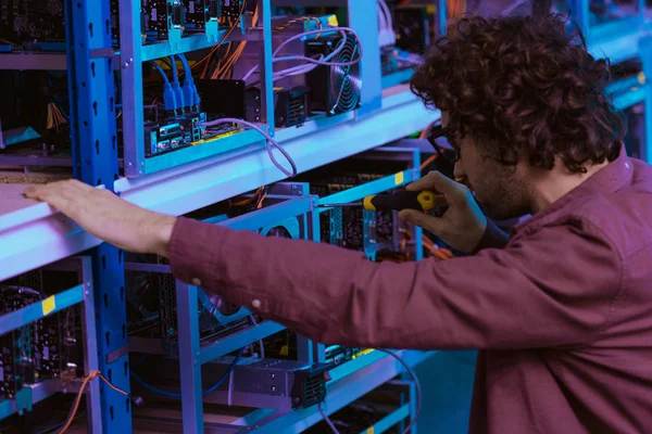 Close-up shot of young computer engineer repairing at ethereum mining farm with screwdriver — Stock Photo