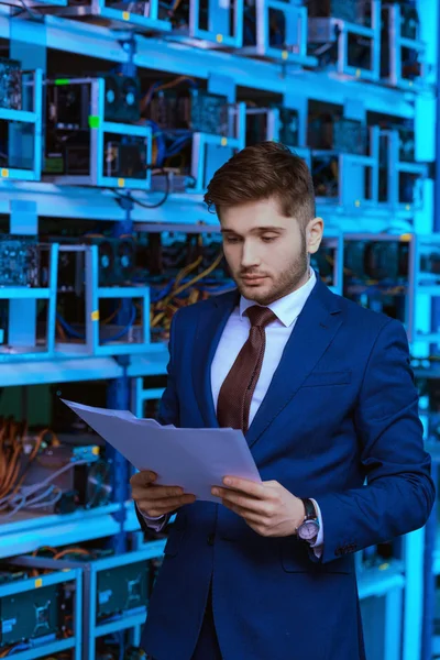 Handsome young businessman reading documents at ethereum mining farm — Stock Photo