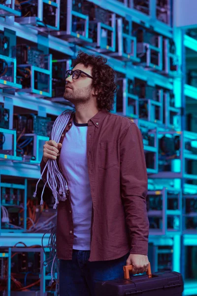 Young computer engineer with wires on shoulder at ethereum mining farm — Stock Photo