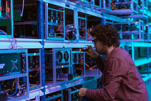 Young computer engineer repairing at cryptocurrency mining farm with screwdriver — Stock Photo