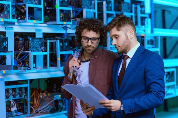 Businessman and computer engineer working with documents together at cryptocurrency mining farm — Stock Photo