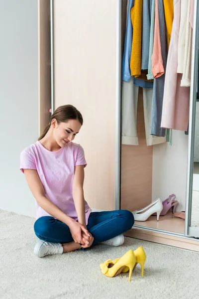 Attraktive junge Frau, die auf dem Boden sitzt und zu Hause auf Schuhe schaut — Stockfoto