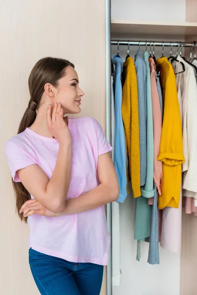 Réfléchie jeune femme regardant les vêtements suspendus dans le cabinet à la maison — Photo de stock