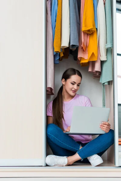 Heureuse jeune femme assise à l'intérieur de l'armoire et travaillant avec ordinateur portable à la maison — Photo de stock