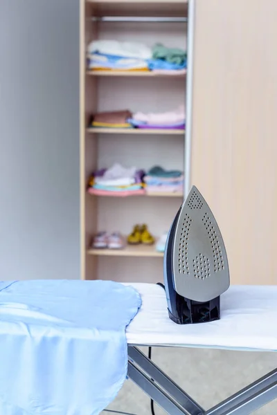 Close-up shot of iron on board in front of cabinet with clothes — Stock Photo