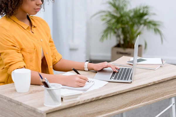 Cropped shot of young woman working with laptop and notebook — Stock Photo
