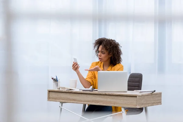 Wütende junge Frau schaut am Arbeitsplatz aufs Smartphone — Stockfoto