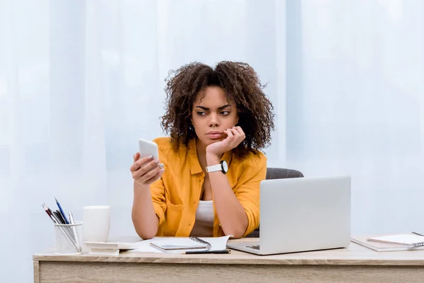 Suspecting young woman looking at smartphone at workplace — Stock Photo