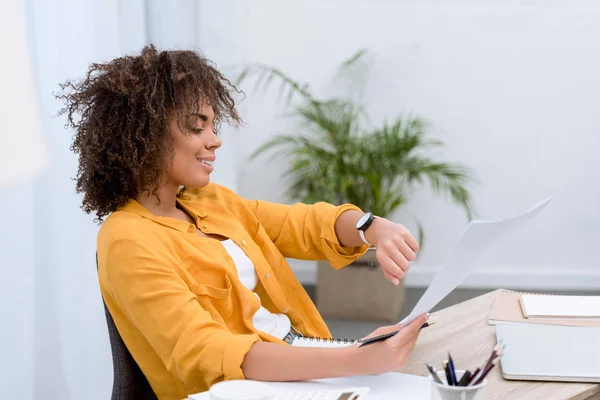 Молодая африканская американка в офисе смотрит на часы — стоковое фото