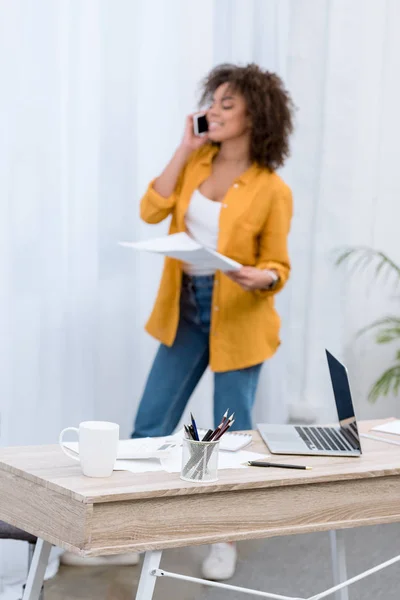 Beautiful young woman talking by phone and reading documents at office — Stock Photo