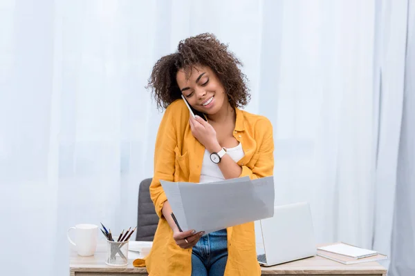 Beautiful young woman talking by phone and reading documents — Stock Photo