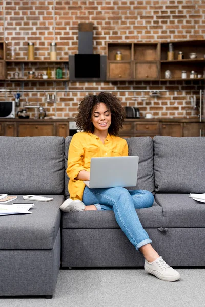 Schöne Mischlingshündin arbeitet mit Laptop auf der Couch — Stockfoto