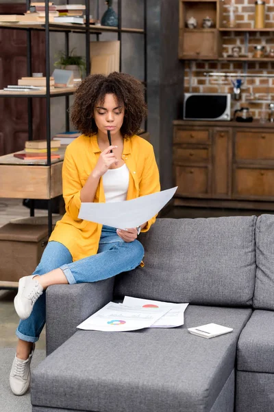 Beautiful young woman doing paperwork at home on couch — Stock Photo
