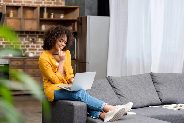 Attrayant jeune femme travaillant avec ordinateur portable à la maison avec cuisine grenier floue sur fond — Photo de stock