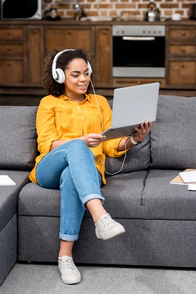 Mujer joven sonriente que trabaja con el ordenador portátil y escucha música en casa - foto de stock