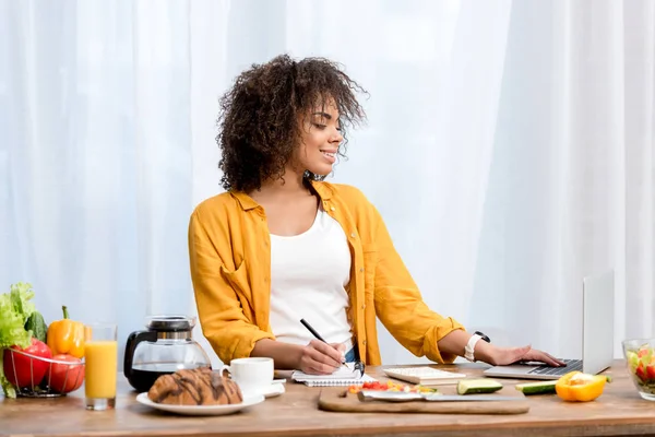 Beautiful young woman working with laptop while taking meal — Stock Photo