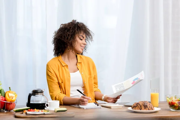 Atractiva mujer afroamericana que trabaja en casa durante el desayuno - foto de stock