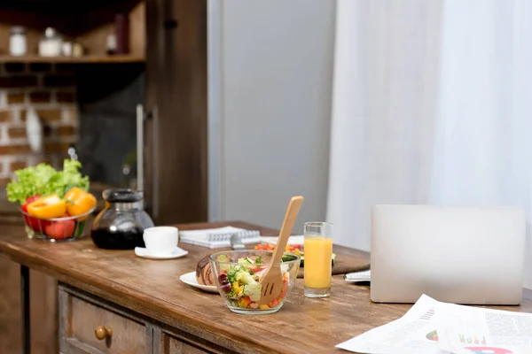 Close-up shot of freelancer workplace at kitchen with food on table and laptop — Stock Photo